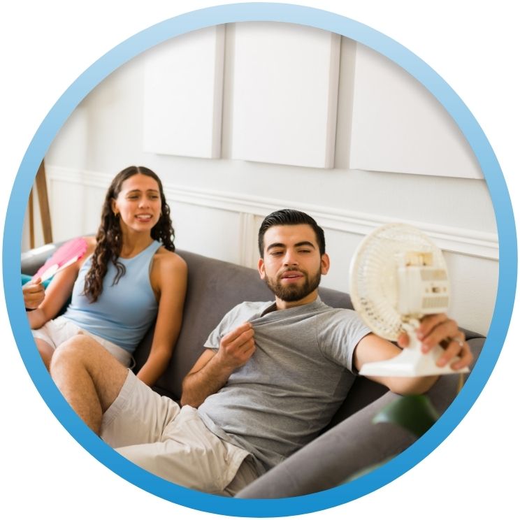 Couple on sofa using a small fan to stay cool.