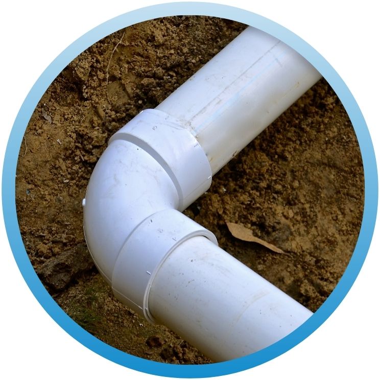 Close-up of a 90-degree white PVC elbow joint in a dirt trench