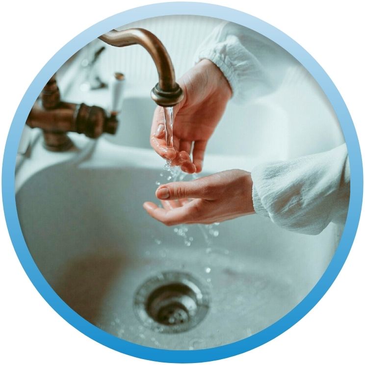 Hands washing in a sink with water swirling toward the drain.
