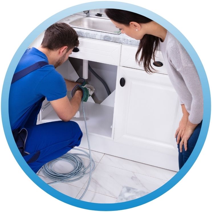 Technician using a motorized drain snake under a kitchen cabinet.