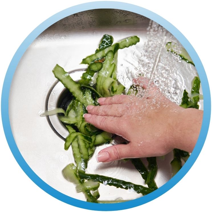 Hand pushing cucumber peels into a stainless steel sink.
