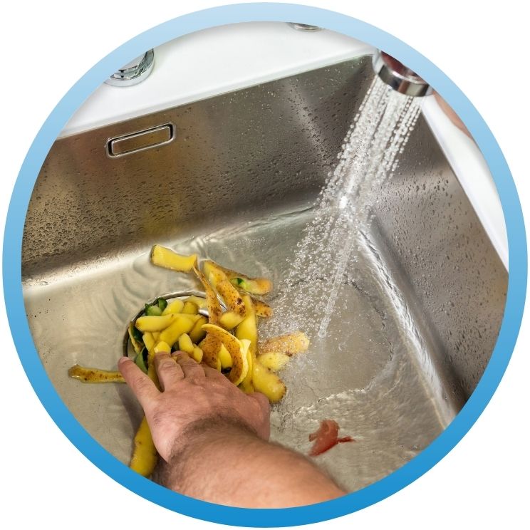 Hand rinsing potato peels into a kitchen sink disposal.