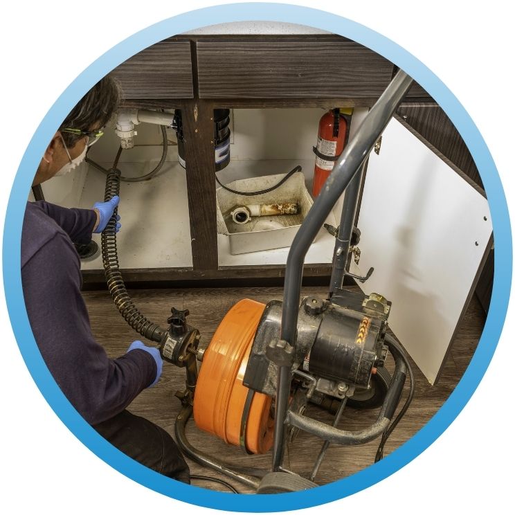 Technician using an orange motorized drain snake under a sink