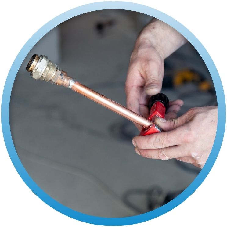 Hands using a red pipe cutter on copper tubing.