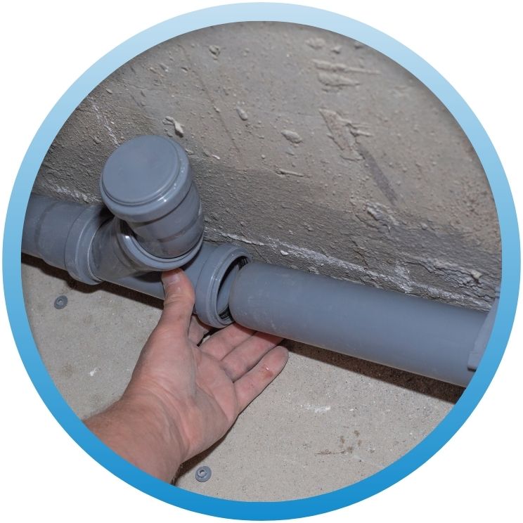 Hand aligning gray PVC drainage pipes against a wall.