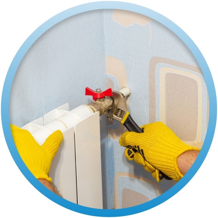 Yellow-gloved hands using a wrench on a radiator valve.