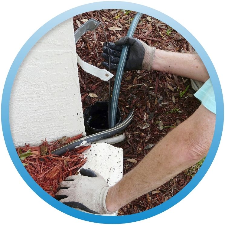 Gloved hands feeding a line into an outdoor drain.