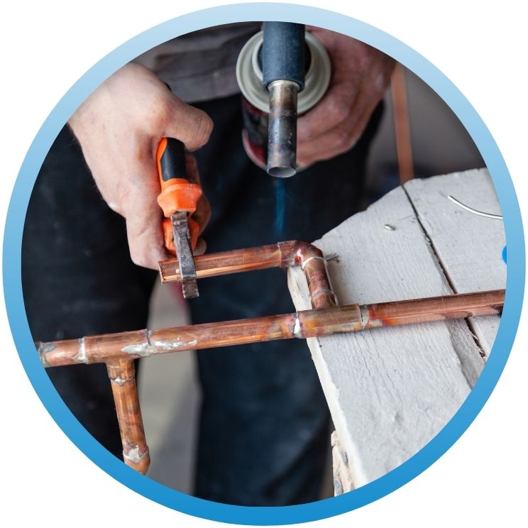 Technician using a blowtorch to solder copper piping.