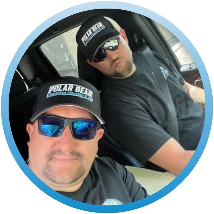 Two plumbing technicians wearing Polar Bear branded apparel inside a vehicle.