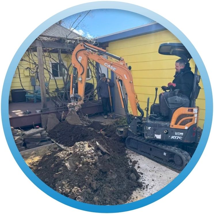 Mini excavator digging a trench beside a yellow house.