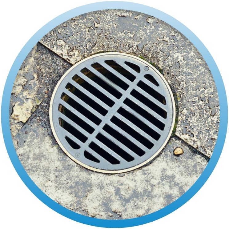 Circular black metal drain grate set in concrete.