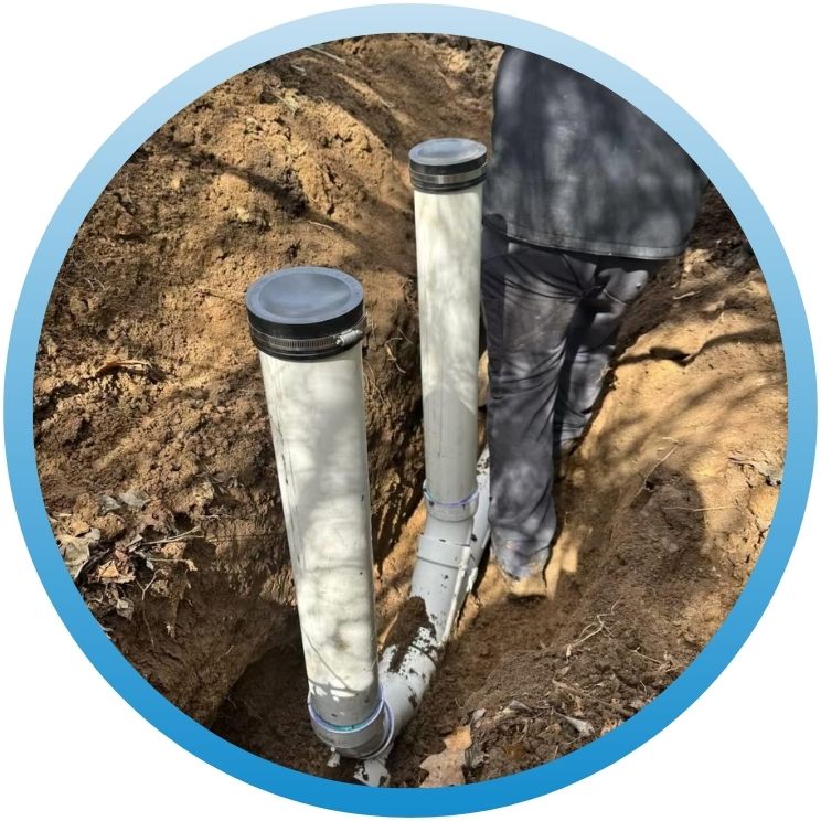 New white PVC vertical cleanouts installed in a dirt trench.