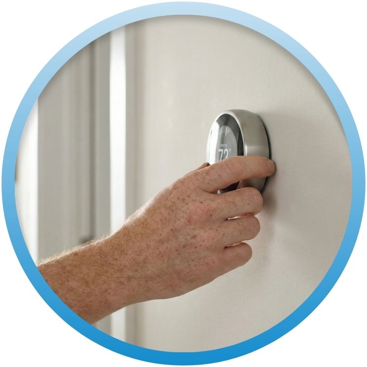 Hand adjusting a sleek, round silver smart thermostat.