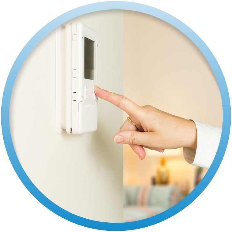 Finger pressing a button on a white digital thermostat.